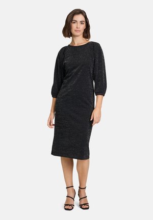 Black, sparkly dress with elbow-length sleeves, a round neckline, and a fitted silhouette, paired with strappy black heels.