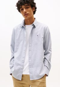 Lichtblauwe button-up shirt met een gestructureerd ruitpatroon, opgerolde mouwen en een klein logo-detail op de borst, gedragen over een wit T-shirt.