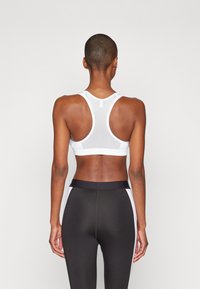 Hvit athletic sports-BH med racerback-design og mesh tekstur. Sammen med høy midje svarte tights med hvite sidepaneler.