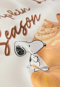Snoopy cartoon character next to embroidered brown text "season" and images of pumpkin and pumpkin spice on white fabric.