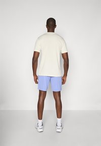 T-shirt de mangas curtas de cor creme clara, combinado com calções azul claros, usado com meias brancas e sapatilhas desportivas, visto pela parte de trás.