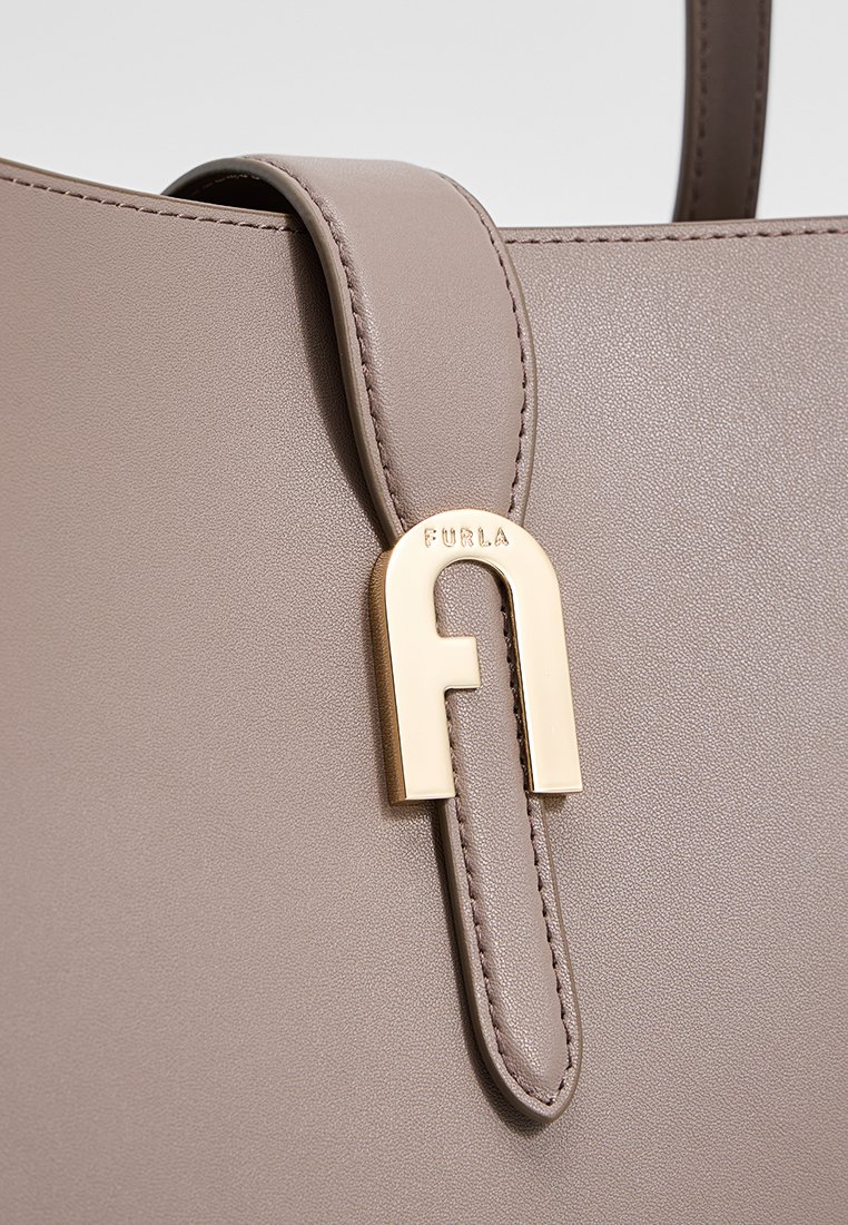 Beige Lederhandtasche mit goldfarbenen Metalldetails und Logo. Glatte Textur und strukturiertes Design mit einem Griff.