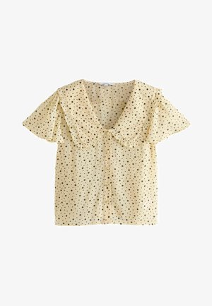 Žlutá blůza s krátkým rukávem a volánkovým límcem, s černými puntíky a zapínáním na knoflíky vpředu. Hladká, lehká tkanina.