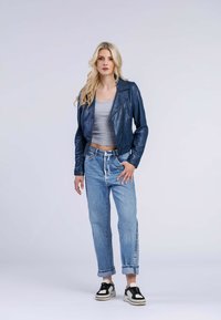 Giacca biker in pelle blu navy, top corto grigio, jeans di denim azzurro chiaro e sneakers nere con suola bianca. Outfit urbano casual.