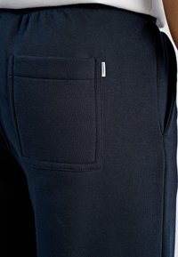 Marineblauwe trainingsbroek met een grote achterzak, zachte textuur, elastische tailleband en een klein merkembleem op de zijnnaad.