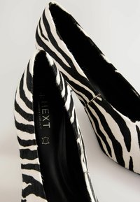 Black and white zebra-striped flat shoes made of textured hair-on material, featuring a pointed toe and a smooth black interior.