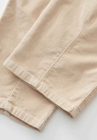 Tissu en velours côtelé beige avec coutures et ourlets visibles, montrant un gros plan de jambes de pantalon pliées.