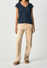 Námořnické v-neck tričko s krátkým rukávem spárované se světle béžovými, volnými kalhotami a hnědými sandály. Tkaniny se zdají být měkké a uvolněné.