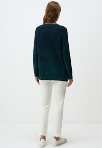 Donkerblauwe gebreide trui met een textuurpatroon, voorzien van een geribbelde zoom en boorden. Gecombineerd met witte strakke broek en witte sneakers.