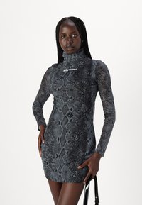 Tamsiai pilka prigludusi ilga suknelė su gyvatės rašto patterned, turinti aukštą apykaklę ir baltą Karl Lagerfeld logotipą.