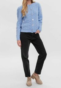 Ljusblå kabelstickad cardigan med rund halsringning och fem knappar, kombinerad med svarta byxor och beige klumpiga skor.