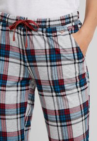 Graue Karohosen mit roten, blauen und schwarzen Mustern. Sie verfügen über einen elastischen Taillenbund mit einem roten Kordelzug und seitlichen Taschen. Weiches Material.