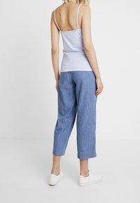 Světle modrý pruhovaný top na tenké ramínka v kombinaci s volnými, světle modrými denimovými kalhotami do poloviny lýtek. Oblečení doplňují bílé tenisky.