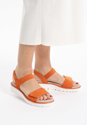 Orange suede sandals with two wide straps, white contoured sole, and textured grip. Open-toe design reveals pedicure.