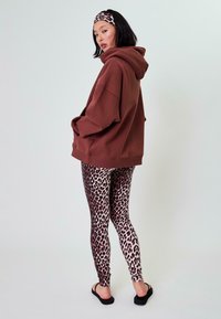 Felpa oversize marrone, leggings con stampa leopardata e una fascia abbinata; vestibilità rilassata, tessuto morbido e motivo animale distintivo. Sandali neri.