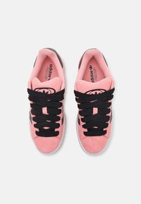 Růžové semišové tenisky s černými tkaničkami a detaily, na jazyku výrazné logo a texturovaná pryžová podrážka.