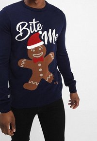 Pull en tricot bleu marine avec un motif de bonhomme en pain d'épice, texte "Bite Me", chapeau rouge et nœud papillon. Texture douce avec des poignets côtelés.