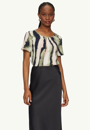 Blouse à imprimé floral en vert, rose et bleu marine, avec des manches courtes et un design plissé, associée à une jupe noire unie longueur cheville.