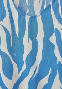 Tessuto a pattern blu e bianco con un design ondulato. La parte superiore presenta una texture liscia e un collo rotondo.