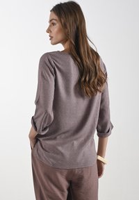 Paarse gebloemde top met lange mouwen en opgerolde mouwen, met een subtiel ontwerp en een gebogen zoom, gecombineerd met bijpassende broek.