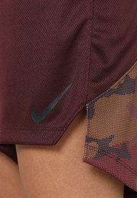 Nike Sportshorts aus tiefrotem Stoff mit strukturiertem Muster, ausgestattet mit einem Camouflage-Mesh-Einsatz und einem schwarzen Logo am Saum.