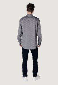 Camisa gris de manga larga con un patrón sutil, cuello con solapa y detalle de botones, combinada con jeans oscuros y zapatillas blancas.
