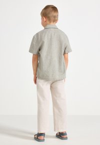 Camisetta a maniche corte di colore grigio chiaro con finitura testurizzata, abbinata a pantaloni beige chiaro morbidi e sandali blu.