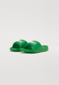 Vihreät liukusandaalit, joissa on sileä kumipinta, avonainen varvasosa ja valkoinen Lacoste-logo. Rakenteellinen pohja tarjoaa pidon ja mukavuuden.