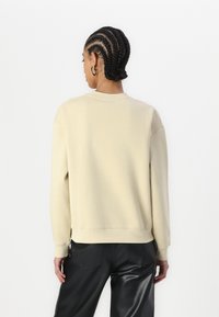 Sudadera beige, cuello redondo, material de algodón, corte relajado, puños y dobladillo acanalados, combinada con pantalones negros, textura suave.