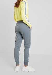 Spårjacka i lysande gult med blå ränder, kombinerad med grå tapered joggers med vita sidodetaljer och ribbade avslut, bärs tillsammans med vita sneakers.