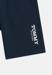 Jūras zila bikses no gludas auduma. Malā ir balta logo uzraksts "TOMMY HILFIGER". Vienkāršs dizains ar tīrām līnijām.