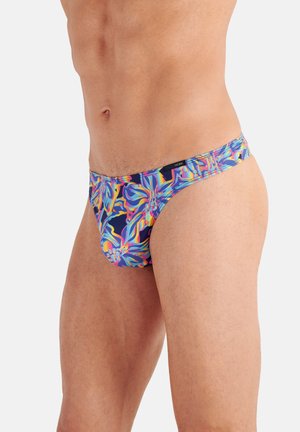 Männlicher Oberkörper mit farbenfroher, floral gemusterter Slips-Unterwäsche vor hellem Hintergrund.