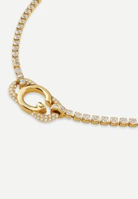 Collana in tono oro con cristalli trasparenti scintillanti, dotata di un design unico della chiusura. La catena è composta da anelli quadrati con accenti di pietra.