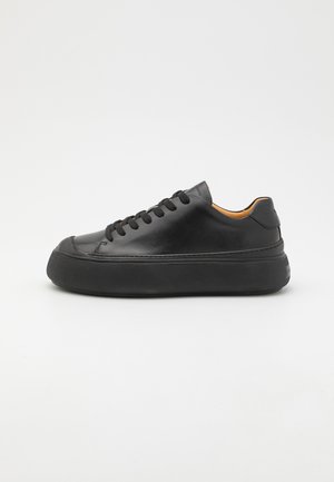 Czarny skórzany niski sneaker z grubą podeszwą i czarnymi sznurówkami na jednolitym białym tle.