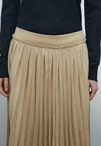 Beige-harma verkko hame, jossa on sileä ja leveä vyötärö. Teksturoitu kangas, jossa on pystysuorat raidat ja hapsureuna. Yhdistetty tumman yläosan kanssa.