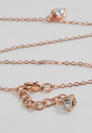 Rosegouden ketting met een karabijnsluiting en een klein rond helder edelsteenbedel vlakbij de sluiting op een witte achtergrond.