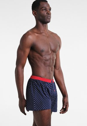 Boxers pour hommes en bleu marine avec des pois blancs, dotés d'une ceinture élastique rouge et d'une coupe décontractée. Tissu doux avec une texture lisse.
