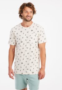 Camisa crema con un acabado texturizado, que presenta un estampado repetido de pequeñas figuras. Incluye un bolsillo en el pecho y mangas cortas.