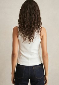 Rippendes weißes Tanktop mit einer taillierten Passform, kombiniert mit dunkelblauen hochgeschnittenen Jeans mit orangefarbenen Nähten und Gesäßtaschen.