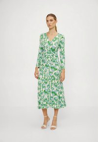 Φόρεμα με μακριά μανίκια και τύπου ντουμπλ απ, με φλοράλ σχέδιο σε πράσινους και μπλε τόνους πάνω σε λευκό φόντο, συμπληρωμένο με φαρδύ τελείωμα και λαιμόκοψη σε σχήμα V.