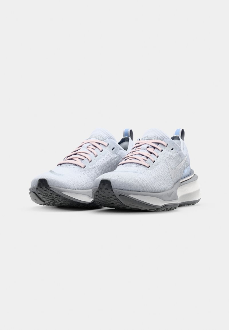 Scarpe sportive grigio chiaro con tomaia in knit testurizzato, lacci rosa, dettagli riflettenti e suola in gomma grigio scuro. Presenta un pratico linguetta sul tallone.