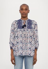 Leichte Bluse mit floralem Muster in Weiß, Marineblau und Rot. Verfügt über einen gemusterten oberen Teil, einen Ausschnitt mit Schlüsselöffnung und Quasten sowie elastische Bündchen.