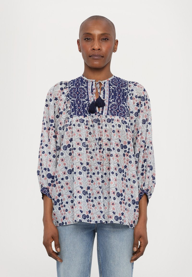 Leichte Bluse mit floralem Muster in Weiß, Marineblau und Rot. Verfügt über einen gemusterten oberen Teil, einen Ausschnitt mit Schlüsselöffnung und Quasten sowie elastische Bündchen.