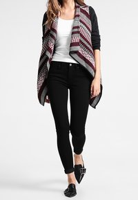 Flerfärgad kofta med röda, grå och vita ränder; kombinerad med svarta skinny jeans och svarta platta skor med spänndetalj.