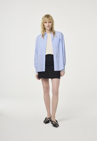 Light blue, striped shirt with long sleeves, buttoned, worn over a cream top. Black mini skirt with lace-up detail and black shoes with studs.