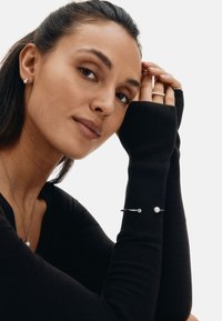 Juodas ilgomis rankovėmis, siaurėjančiomis sijonėlio rankogaliais. Sidabrinė apyrankė su perlu ir skaidriu akmeniu. Matomas minimalistinis vėrinys. Minkšta audinio tekstūra.