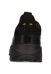 Schwarze Wildledersneaker mit einer dicken schwarzen Gummisohle, die gelbe Akzente und eine Zuglasche an der Ferse für ein einfaches Anziehen aufweist.