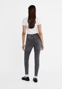 Jeans ajustados de mezclilla gris con cintura alta, bolsillos traseros y un acabado desgastado; combinados con una camiseta blanca ajustada y zapatos negros.