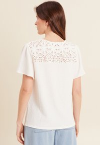 Witte textuur korte mouwen blouse met een gedetailleerde haakwerk achterkant en een ronde halslijn, geschikt voor casual draag.