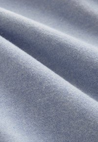 Tejido de algodón azul claro con una textura suave, que presenta un tejido fino y un brillo sutil. La superficie está ligeramente arrugada.